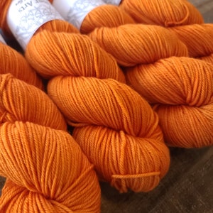 May include: Close-up of several skeins of vibrant orange yarn. The yarn is tightly wound, showing the texture of the fibers. The color is a rich, warm orange, perfect for knitting or crocheting projects. The yarn is labeled with the text "Sweet Arts".