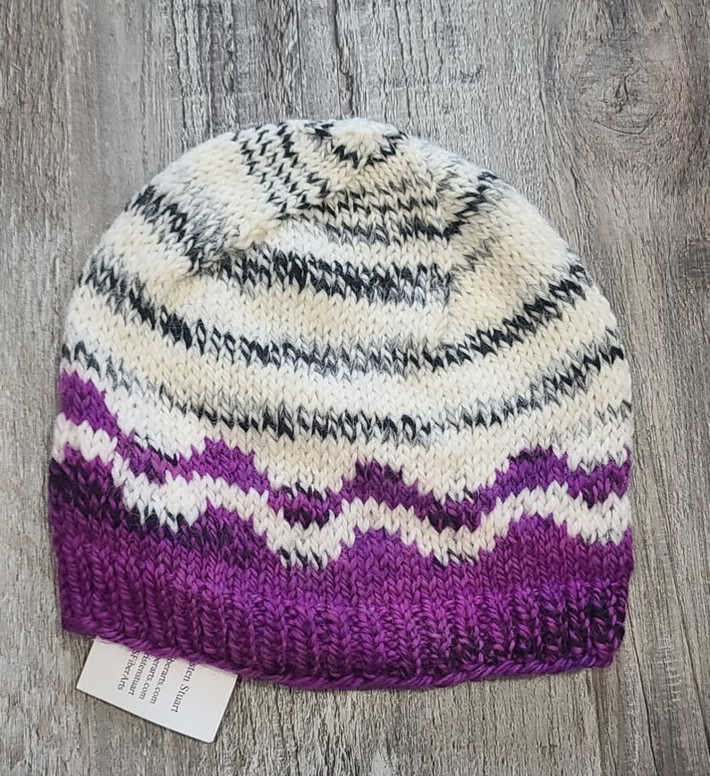 May include: A purple, white, and black striped knitted hat with a wavy pattern. The hat is made of wool and has a soft, comfortable feel.