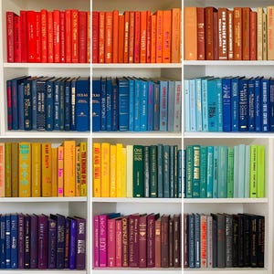 May include: A bookshelf filled with colourful books, organised by colour. The books are arranged in rows, with each row featuring a different colour. The colours include red, orange, yellow, green, blue, purple, and black.