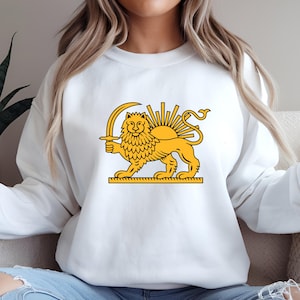 May include: White sweatshirt with a yellow lion holding a sword, and a sun and rays design. The lion stands on a rectangular base. The design is centred on the front of the sweatshirt.