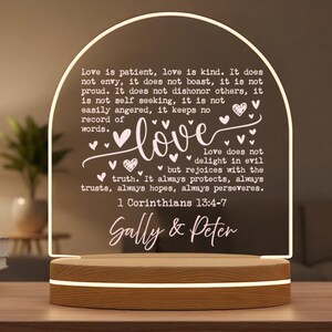 May include: An LED night light with a wooden base and a clear, arched top. The top displays the word "love" and a Bible verse about love, with the names "Sally & Peter" below. The light emits a warm glow.