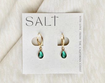 May include: Gold-tone hoop earrings with teardrop-shaped, emerald green gemstones. The earrings are displayed on a white card with the word "SALT" and the phrase "WITH LOVE FROM THE CALIFORNIA COAST".