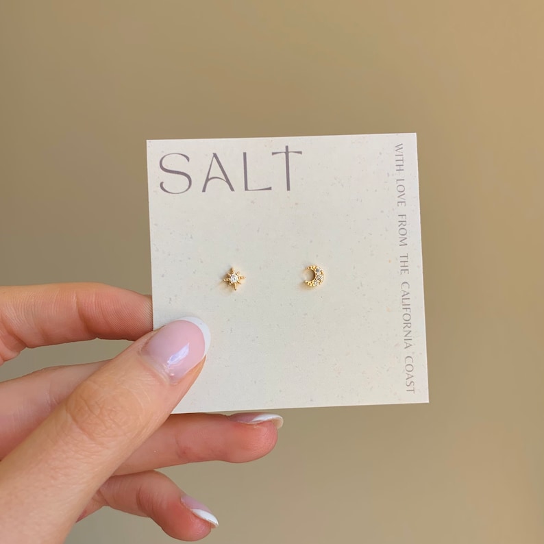 Dainty gold star and moon stud earrings with sparkling cubic zirconia stones, displayed on a neutral-toned 'SALT' jewelry card. These start and moon minimalist celestial earrings are perfect for everyday wear or gifting.