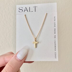 May include: A gold-colored cross pendant necklace on a white card with the word "SALT" at the top. The necklace is displayed on a white card with the text "WITH LOVE FROM THE CALIFORNIA COAST".