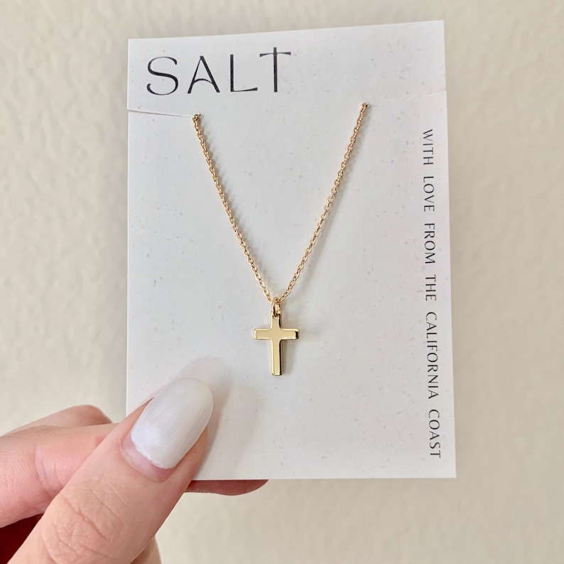 May include: A gold-colored cross pendant necklace on a white card with the word "SALT" at the top. The necklace is displayed on a white card with the text "WITH LOVE FROM THE CALIFORNIA COAST".