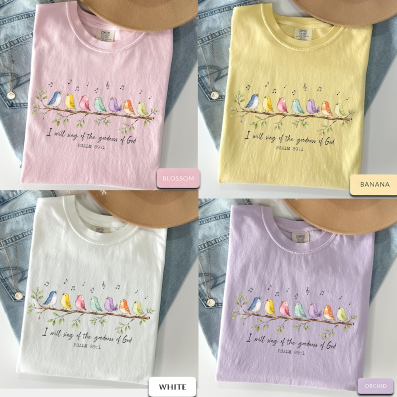 May include: Four short-sleeve t-shirts in blossom pink, banana yellow, white, and orchid purple. Each shirt features a graphic of seven colorful birds perched on a branch with musical notes and the text I will sing of the goodness of God PSALM 89:1.