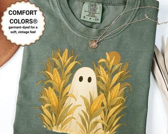 May include: Green Comfort Colors t-shirt featuring a ghost in a cornfield design. The shirt has a round neckline and short sleeves. The text "COMFORT COLORS® garment-dyed for a soft, vintage feel" is on the left side of the shirt.