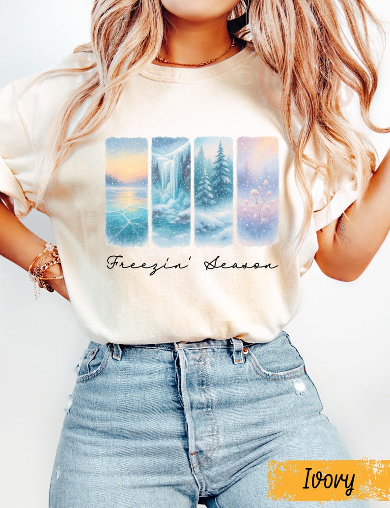 Puede incluir: Sudadera de color marfil con un dise&ntilde;o de paisaje invernal. Cuatro paneles verticales muestran escenas nevadas: un lago, una cascada y &aacute;rboles. Las palabras "Freezin' Season" est&aacute;n escritas en cursiva debajo.