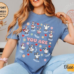 May include: Blue jean coloured t-shirt featuring cartoon geese and the words "YOU ARE" surrounded by positive affirmations. The garment-dyed shirt has a soft, vintage feel.