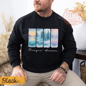 May include: Black sweatshirt with a winter landscape design. The design features four vertical panels with scenes of ice, waterfalls, and snowy trees. The words "Freezin' Season" are written in cursive below the panels.