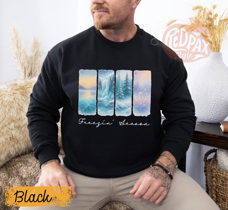 May include: Black sweatshirt with a winter landscape design. The design features four vertical panels with scenes of ice, waterfalls, and snowy trees. The words "Freezin' Season" are written in cursive below the panels.