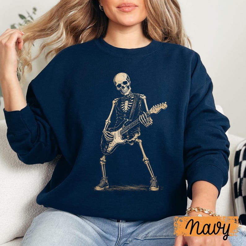 Peut inclure: Un sweat-shirt bleu marine &agrave; col rond avec une impression graphique repr&eacute;sentant un squelette portant un gilet et un n&oelig;ud papillon tout en jouant de la guitare &eacute;lectrique. Le squelette est beige clair, debout en position &eacute;cart&eacute;e avec des baskets.