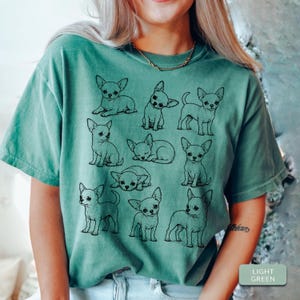 May include: A light green short-sleeve t-shirt featuring a black line art graphic print of nine different Chihuahua dogs in various poses, including sitting, standing, and lying down, arranged in a grid-like pattern across the front.