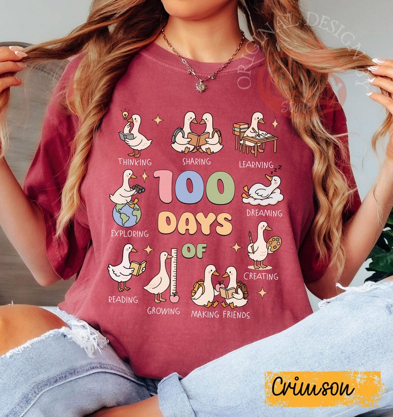 May include: Crimson-colored t-shirt with a colorful graphic celebrating "100 Days Of" learning. The design features cartoon geese engaged in various activities like reading, sharing, and exploring. The text "Crimson" is at the bottom.