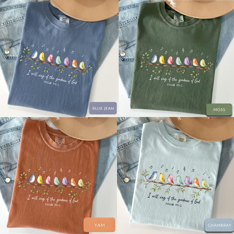 May include: A collection of four crew neck t-shirts in blue jean, moss, yam, and chambray colors. Each shirt features a graphic of eight colorful birds perched on a branch with musical notes and the text I will sing of the goodness of God Psalm 89:1.
