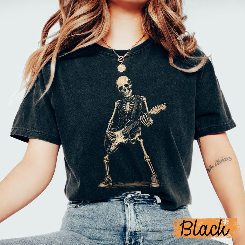 Peut inclure: Un t-shirt noir &agrave; manches courtes avec une impression graphique repr&eacute;sentant un squelette portant un gilet et un n&oelig;ud papillon tout en jouant de la guitare &eacute;lectrique. Le squelette est debout, porte des baskets, et le motif est en beige.