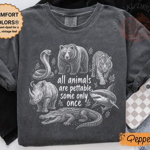 Op de afbeelding: Een antracietgrijs t-shirt met korte mouwen en een witte grafische print van een slang, beer, tijger, neushoorn, haai en krokodil. De tekst luidt "all animals are pettable, some only once". Het shirt heeft een ronde hals en een vintage wassing.