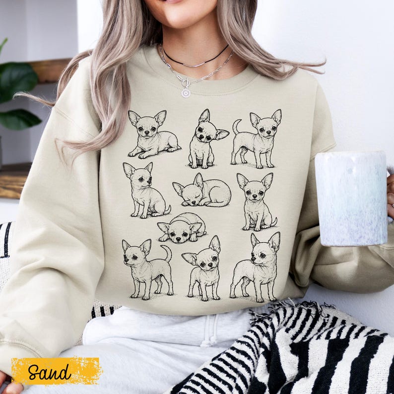 May include: A sand-colored crewneck sweatshirt featuring a graphic print of nine black and white line art illustrations of Chihuahua dogs in various poses, including sitting, standing, and lying down, arranged in a grid pattern on the front.