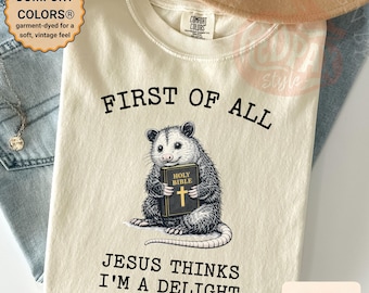 Può includere: T-shirt color avorio con la scritta "FIRST OF ALL" e "JESUS THINKS I'M A DELIGHT". La maglietta presenta una grafica di un opossum che tiene in mano una Bibbia. Il capo è tinto per una sensazione morbida e vintage.