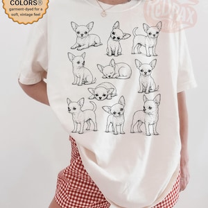 May include: An ivory t-shirt featuring a black line art graphic of ten different Chihuahua dogs in various poses. The shirt includes a circular badge in the top left corner with the text COMFORT COLORS garment-dyed for a soft, vintage feel.