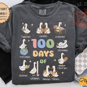 May include: Dark gray long-sleeve shirt with a colorful graphic celebrating "100 Days of School." The design features cartoon geese engaged in various activities like reading and creating. The shirt has the text "COMFORT COLORS&reg;" and "ORIGINAL DESIGN Style".