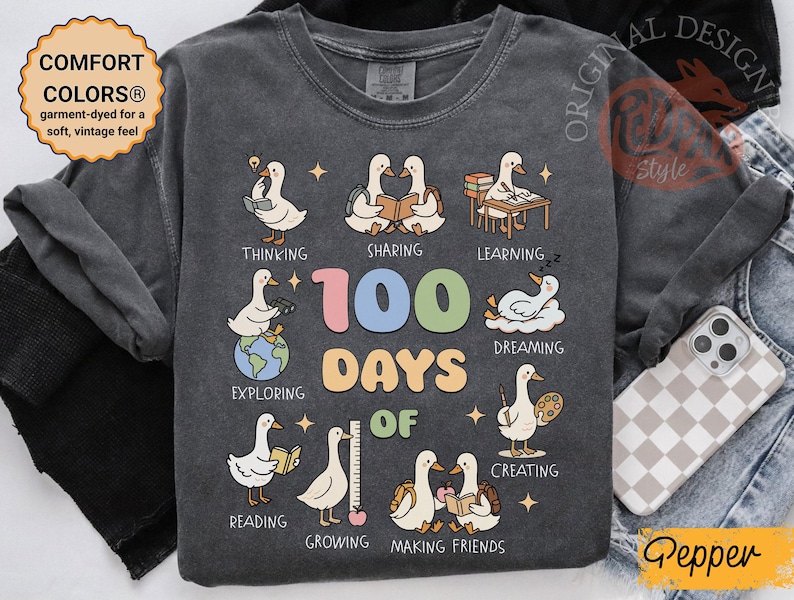 May include: Dark gray long-sleeve shirt with a colorful graphic celebrating "100 Days of School." The design features cartoon geese engaged in various activities like reading and creating. The shirt has the text "COMFORT COLORS&reg;" and "ORIGINAL DESIGN Style".