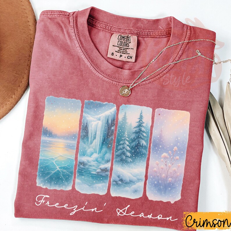 Puede incluir: Camiseta de color carmes&iacute; con un dise&ntilde;o de paisaje invernal. El gr&aacute;fico presenta cuatro paneles rectangulares que representan escenas nevadas, incluyendo un lago helado, una cascada y &aacute;rboles cubiertos de nieve. El texto "Freezin' Season" est&aacute; impreso debajo.