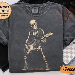 Peut inclure: Un t-shirt &agrave; manches courtes gris anthracite avec un motif de squelette portant un gilet et un n&oelig;ud papillon tout en jouant de la guitare &eacute;lectrique. Le t-shirt a un col rond et un aspect d&eacute;lav&eacute; vintage. Le texte COMFORT COLORS est visible.