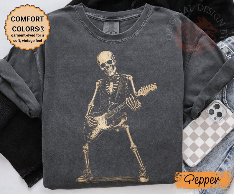 Peut inclure: Un t-shirt &agrave; manches courtes gris anthracite avec un motif de squelette portant un gilet et un n&oelig;ud papillon tout en jouant de la guitare &eacute;lectrique. Le t-shirt a un col rond et un aspect d&eacute;lav&eacute; vintage. Le texte COMFORT COLORS est visible.