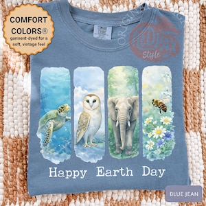 May include: Blue jean colored t-shirt with a watercolor design featuring a sea turtle, owl, elephant, and bee. The words "Happy Earth Day" are printed below the images. The shirt is garment-dyed for a soft, vintage feel.
