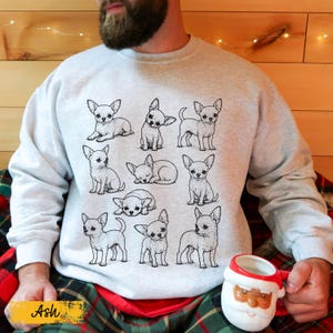 May include: A light gray crewneck sweatshirt featuring a black line art illustration of ten different Chihuahua dogs in various poses, including sitting, standing, and sleeping, printed on the front of the garment.