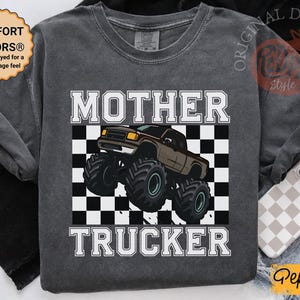 以下が含まれることがあります： 「MOTHER TRUCKER」の文字が白でプリントされた、濃いグレーの長袖シャツ。茶色のモンスターカーのグラフィックが、白と黒のチェック柄の背景に配置されています。このシャツはヴィンテージ感があります。