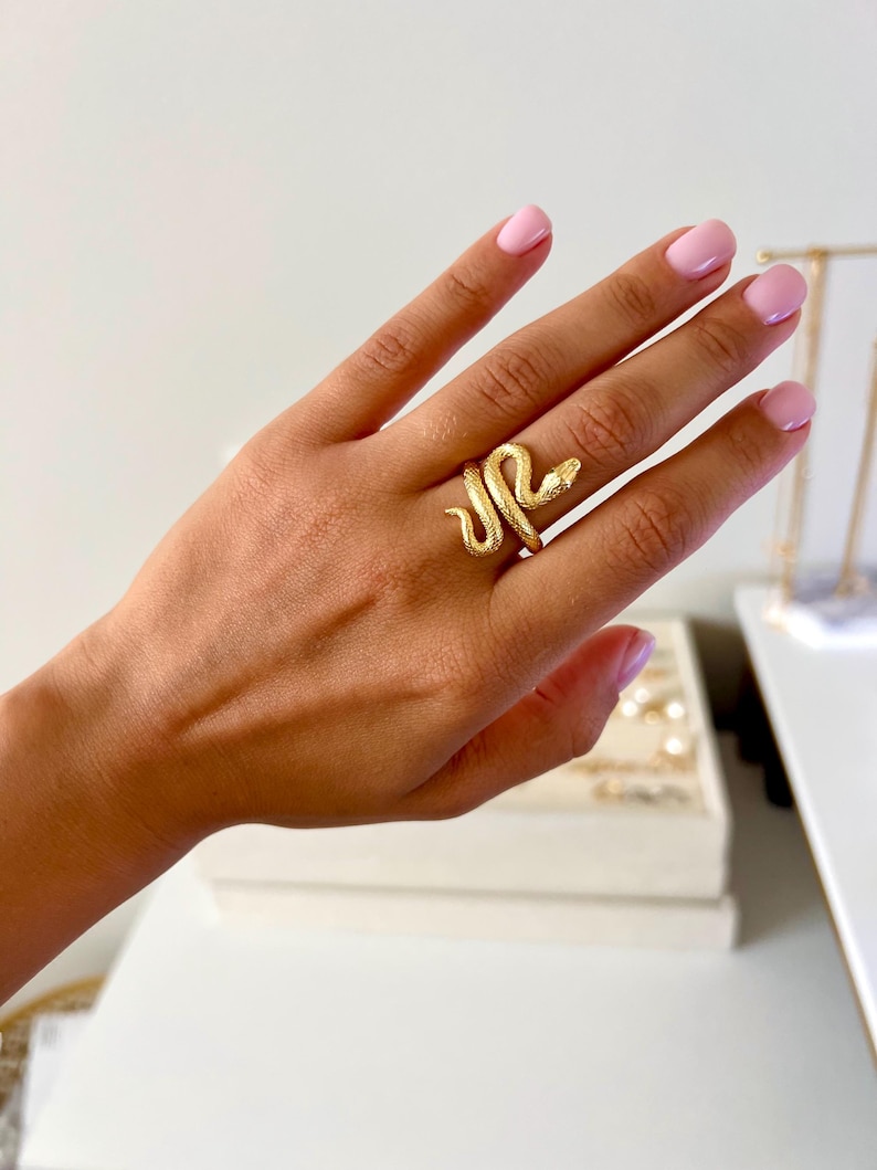 May include: A gold-toned snake ring with a textured finish. The snake is coiled around the ring band and has a raised head.