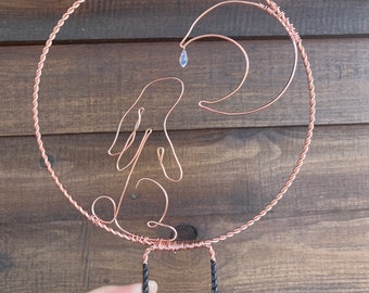 May include: A copper wire sculpture of a rabbit and crescent moon with a crystal hanging from the moon. The sculpture is attached to two black metal rods.