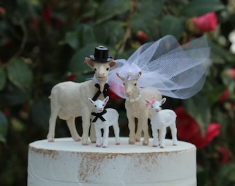 Può includere: Topper per torta nuziale in ceramica bianca con due capre, uno sposo con un cappello a cilindro nero e una sposa con un velo. Lo sposo indossa un papillon nero e la sposa un fiocco bianco. Ci sono due piccole figurine di capre bianche con fiocchi neri.