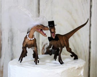 May include: A wedding cake topper featuring a brown dinosaur wearing a white veil and a brown dinosaur wearing a black top hat and bow tie.