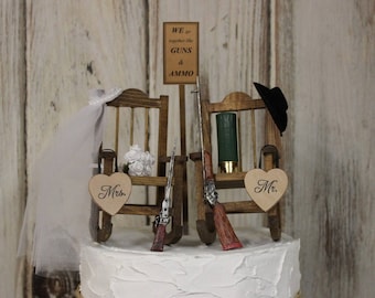 Könnte beinhalten: Ein Hochzeitstortenaufsatz mit zwei Holz-Schaukelstühlen, einem Schild mit der Aufschrift "We go together like guns & ammo", zwei Spielzeugpistolen und zwei herzförmigen Schildern mit der Aufschrift "Mr." und "Mrs."