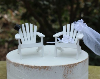 May include: White wooden chairs with a black top hat on one chair and a white veil on the other chair. The chairs are on a white cake.