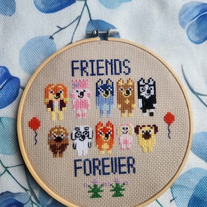 Könnte beinhalten: Ein Kreuzstich-Stickrahmen mit den Worten „FRIENDS FOREVER“ und einer Reihe von zehn Cartoon-Hunden in verschiedenen Farben. Zwei rote Ballons flankieren das Design. Der Rahmen ist aus Holz.