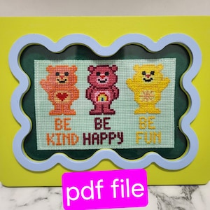 May include: A framed cross-stitch design featuring three Care Bears with the words "Be Kind", "Be Happy", and "Be Fun" underneath each bear.