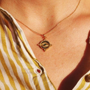 May include: A gold necklace with a pendant shaped like a four-pointed star with an eye in the center. The eye is green and the star has a textured surface.