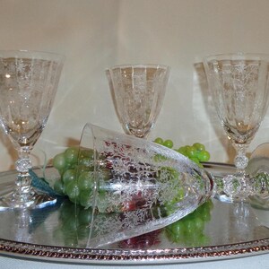 May include: A silver serving tray holds three etched crystal wine glasses and a fallen glass, with green grapes. The glasses have a delicate floral pattern. The tray has a decorative beaded edge, creating an elegant presentation.