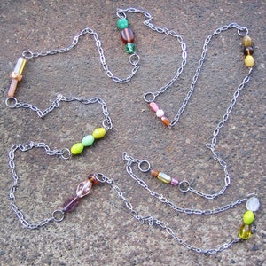 May include: A silver chain necklace with multiple strands and colourful glass beads. The beads are green, yellow, brown, pink and orange.