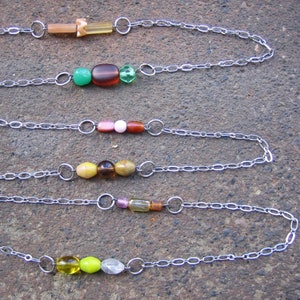 May include: Five silver chains with different coloured beads. The beads are green, brown, pink, yellow, and clear.
