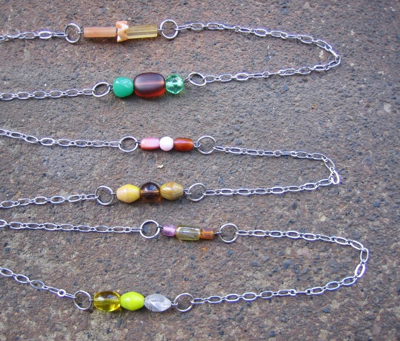 May include: Five silver chains with different coloured beads. The beads are green, brown, pink, yellow, and clear.