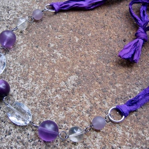 K&ouml;nnte beinhalten: Eine violette und klare Glasperlenkette mit einer violetten Schleife. Die Kette besteht aus abwechselnd klaren und violetten runden Perlen.
