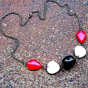 May include: A necklace featuring a dark metallic chain with five smooth, rounded beads in a repeating pattern of red, white, and black. The beads are arranged asymmetrically along the lower portion of the chain, which includes a lobster claw clasp.