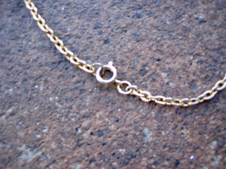 May include: A gold-toned metal chain necklace featuring a circular spring ring clasp mechanism. The chain consists of small, interconnected oval links that form a continuous loop, with the clasp serving as the primary point of connection.