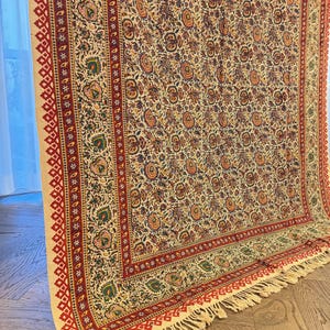 May include: A cream-colored textile with a detailed floral pattern in shades of red, orange, green, and blue. The border features a red geometric design and fringe. This decorative textile is suitable for a variety of uses.