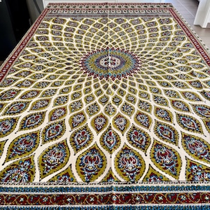 Puede incluir: Un gran tapiz de color crema con un diseño simétrico intrincado. El patrón presenta un medallón central con motivos florales radiantes en tonos de verde, rojo, azul y dorado. El borde es de color rojo oscuro con un patrón repetitivo.